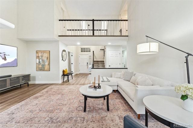 living area with baseboards, visible vents, a high ceiling, and wood finished floors