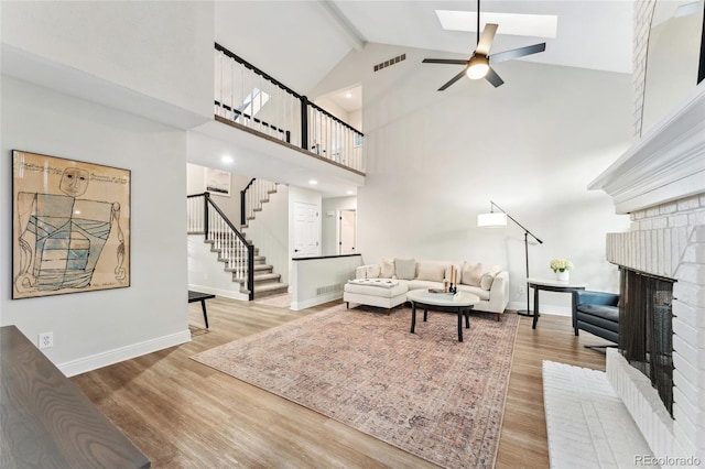 living area with stairs, wood finished floors, high vaulted ceiling, a brick fireplace, and beamed ceiling