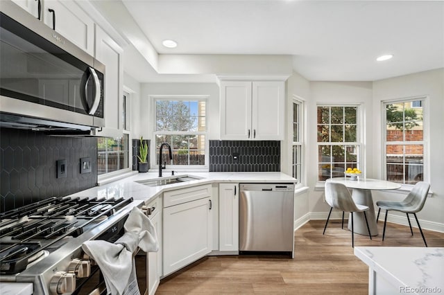 kitchen with recessed lighting, light wood finished floors, a sink, decorative backsplash, and stainless steel appliances
