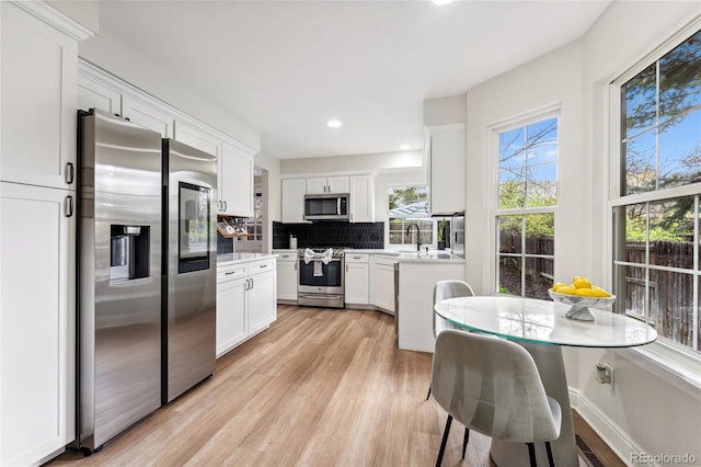 kitchen with a sink, stainless steel appliances, white cabinets, light wood-style floors, and tasteful backsplash