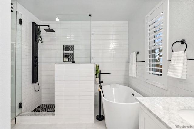 bathroom with tile walls, vanity, a tile shower, and a freestanding tub