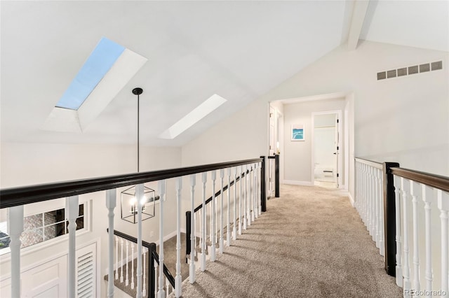 hall featuring carpet flooring, an upstairs landing, visible vents, and vaulted ceiling with skylight