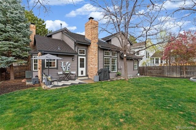 rear view of property featuring a yard, a chimney, a patio area, and a fenced backyard