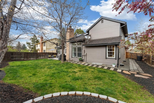 rear view of house with a yard, a patio, a fenced backyard, a chimney, and a shingled roof