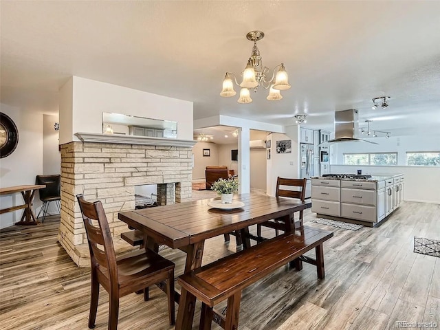 9910 Ammons Cir, Westminster, CO 80021 - dining room featuring a chandelier, a stone fireplace, light wood-type flooring, and baseboards