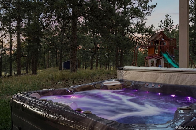 pool at dusk featuring a playground and a hot tub