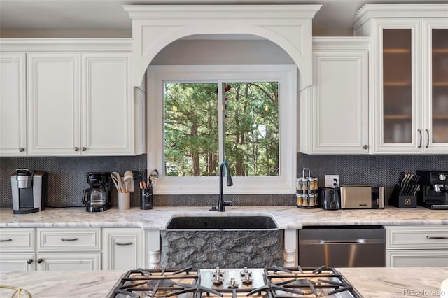 kitchen with light stone countertops, white cabinets, dishwasher, and sink