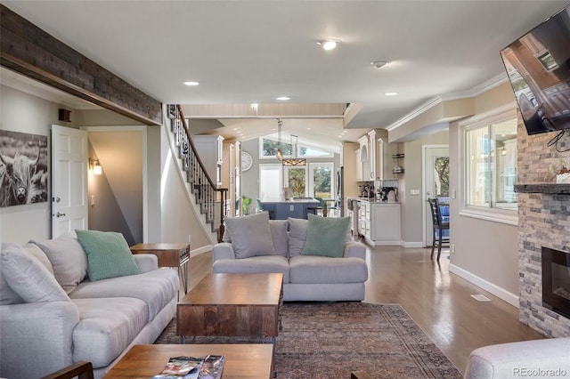 living room featuring ornamental molding, a stone fireplace, vaulted ceiling, a notable chandelier, and hardwood / wood-style floors