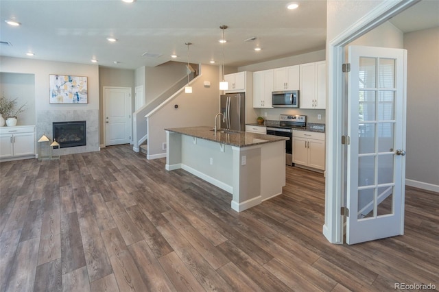 kitchen with appliances with stainless steel finishes, a breakfast bar, white cabinetry, a kitchen island with sink, and dark stone countertops