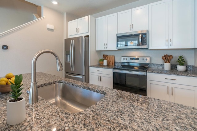 kitchen with appliances with stainless steel finishes, white cabinetry, dark stone counters, and sink