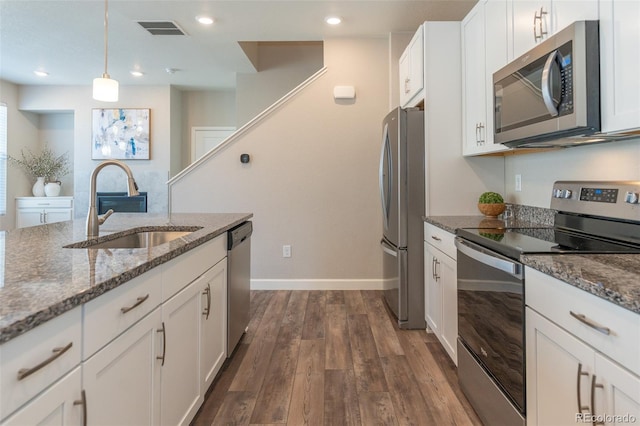 kitchen featuring appliances with stainless steel finishes, sink, pendant lighting, dark stone counters, and white cabinets