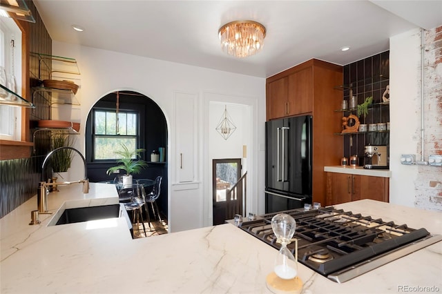 kitchen with sink, light stone counters, high end black fridge, stainless steel gas stovetop, and a chandelier