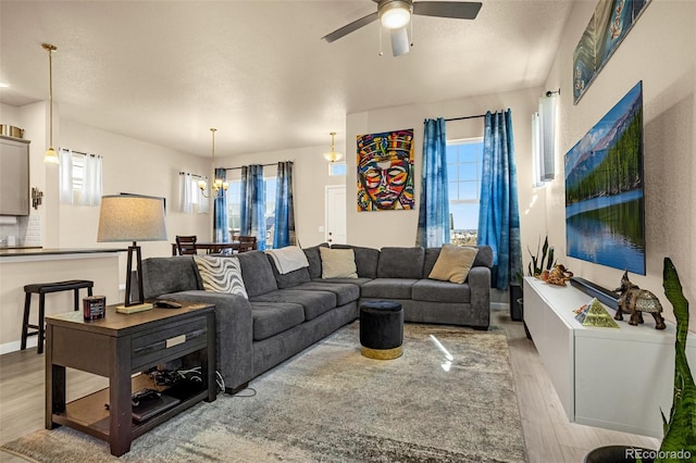 living room featuring ceiling fan with notable chandelier, a textured ceiling, and light hardwood / wood-style flooring