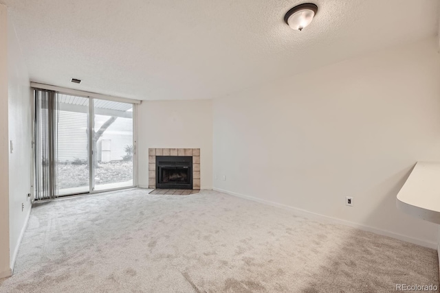 unfurnished living room with a textured ceiling, carpet floors, floor to ceiling windows, and a tiled fireplace