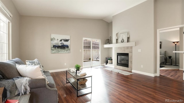 living room with lofted ceiling, a tiled fireplace, and dark wood-type flooring