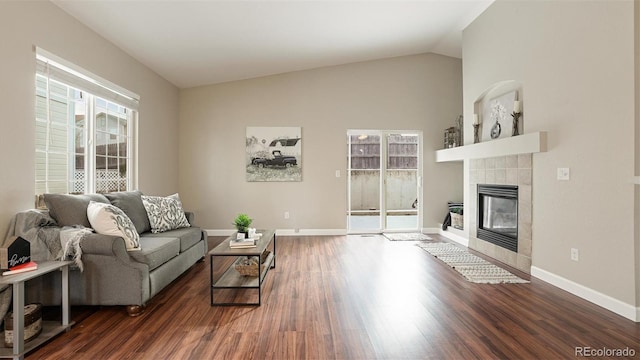 living room with a tiled fireplace, vaulted ceiling, and dark hardwood / wood-style flooring