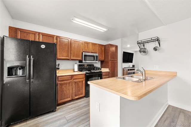 kitchen with black appliances, light hardwood / wood-style floors, kitchen peninsula, and sink