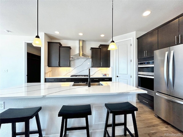 kitchen featuring wall chimney exhaust hood, sink, decorative light fixtures, light hardwood / wood-style flooring, and appliances with stainless steel finishes