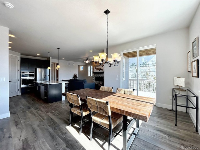 dining space with sink, dark wood-type flooring, a wealth of natural light, and ceiling fan with notable chandelier