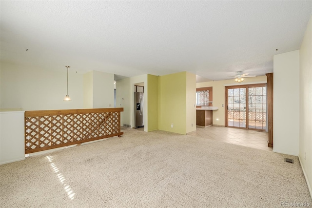 empty room with light tile patterned floors, visible vents, ceiling fan, a textured ceiling, and light carpet