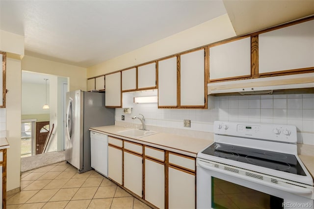 kitchen featuring a sink, under cabinet range hood, tasteful backsplash, white appliances, and light countertops