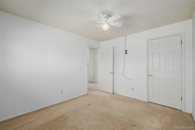 unfurnished bedroom featuring baseboards, light carpet, a textured ceiling, and a ceiling fan