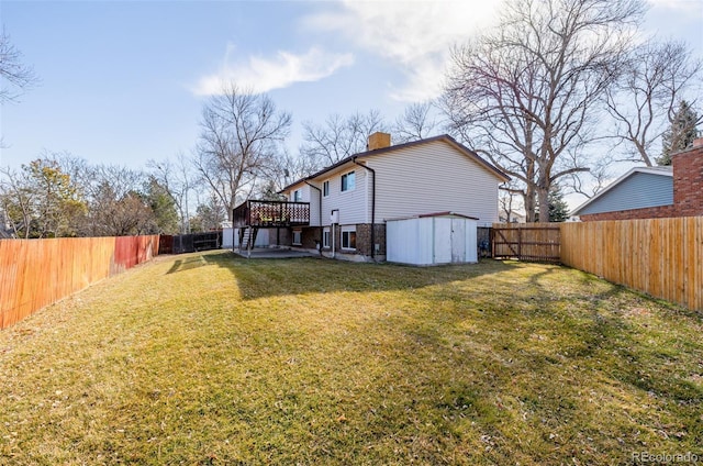 back of house with a chimney, a yard, a deck, a fenced backyard, and an outdoor structure