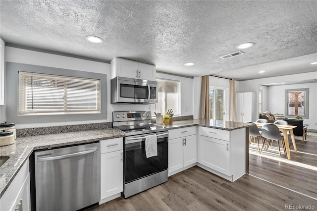 kitchen with appliances with stainless steel finishes, dark hardwood / wood-style floors, stone countertops, and white cabinets