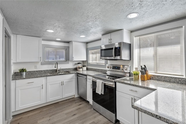 kitchen with sink, appliances with stainless steel finishes, dark stone countertops, light hardwood / wood-style floors, and white cabinets