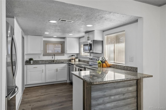 kitchen featuring sink, dark stone countertops, white cabinetry, stainless steel appliances, and kitchen peninsula