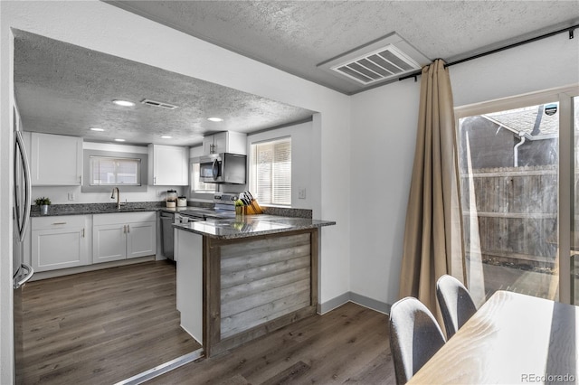 kitchen featuring white cabinetry, dark stone countertops, dark hardwood / wood-style floors, kitchen peninsula, and stainless steel appliances