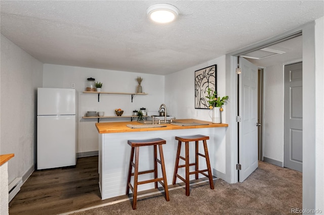 kitchen with wood counters, a kitchen bar, a textured ceiling, white refrigerator, and kitchen peninsula