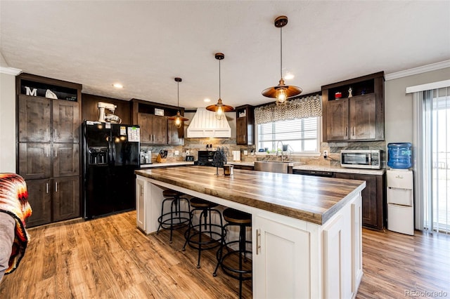 kitchen featuring decorative light fixtures, sink, a center island, dark brown cabinetry, and black refrigerator with ice dispenser