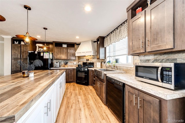 kitchen with pendant lighting, sink, dark brown cabinetry, black appliances, and custom range hood