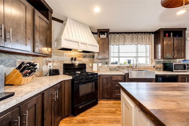 kitchen featuring sink, black range with gas stovetop, backsplash, custom range hood, and light wood-type flooring