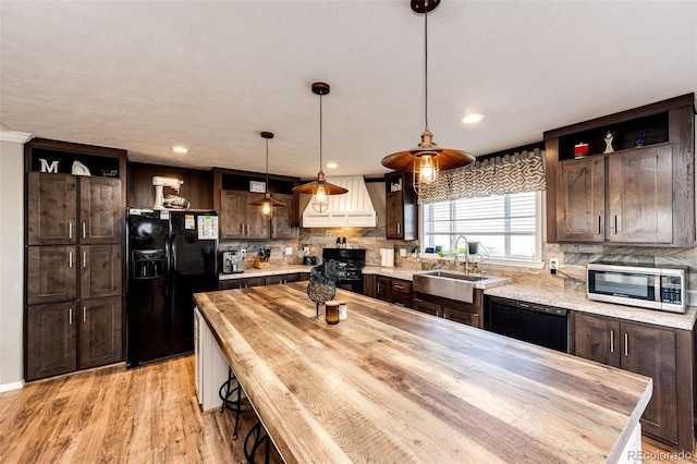 kitchen featuring dark brown cabinetry, sink, hanging light fixtures, custom range hood, and black appliances