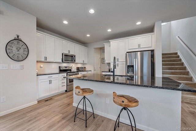 kitchen featuring sink, stainless steel appliances, white cabinets, and a center island with sink