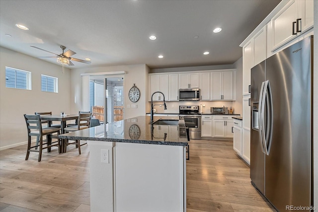 kitchen with sink, a kitchen island with sink, white cabinetry, dark stone countertops, and stainless steel appliances