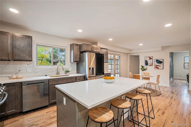 kitchen with stainless steel appliances, sink, a center island, a kitchen bar, and light hardwood / wood-style floors