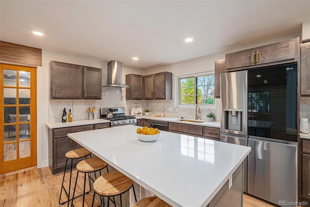 kitchen with wall chimney exhaust hood, light hardwood / wood-style flooring, sink, a center island, and appliances with stainless steel finishes