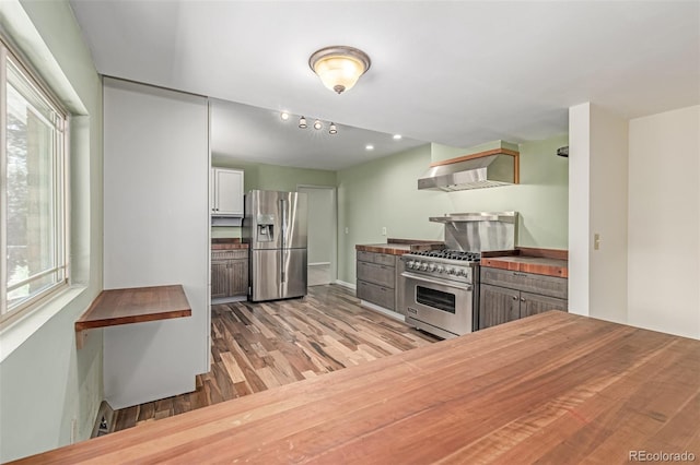 305 Titan St, Aurora, CO 80011 - kitchen featuring appliances with stainless steel finishes, wooden counters, wall chimney range hood, and plenty of natural light