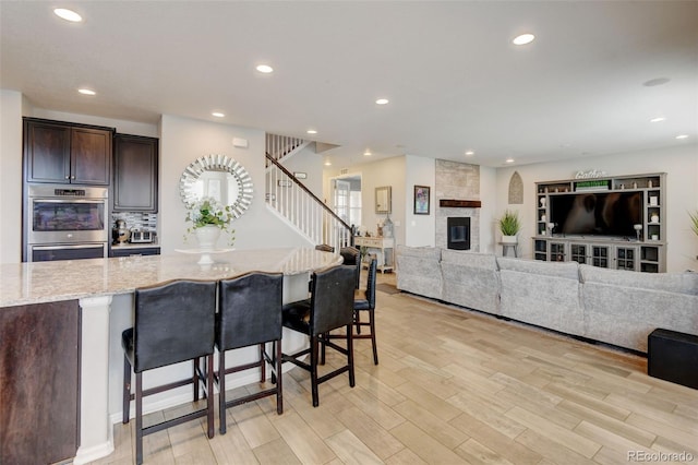 8071 Tabor St, Arvada, CO 80005 - kitchen featuring a breakfast bar, light stone countertops, dark brown cabinets, double oven, and recessed lighting
