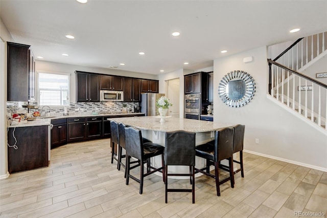 8071 Tabor St, Arvada, CO 80005 - kitchen featuring appliances with stainless steel finishes, a breakfast bar, tasteful backsplash, dark brown cabinetry, and a center island