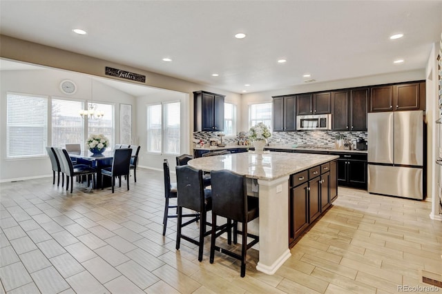 8071 Tabor St, Arvada, CO 80005 - kitchen with appliances with stainless steel finishes, backsplash, a center island, a kitchen breakfast bar, and recessed lighting
