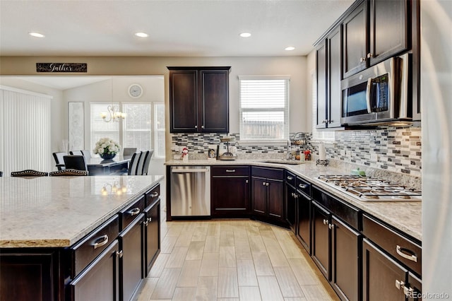 8071 Tabor St, Arvada, CO 80005 - kitchen featuring stainless steel appliances, backsplash, light stone countertops, a chandelier, and dark brown cabinetry