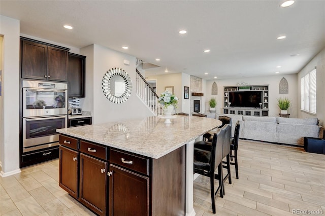 8071 Tabor St, Arvada, CO 80005 - kitchen with double oven, light stone countertops, a kitchen island, open floor plan, and a breakfast bar area