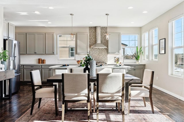 kitchen featuring dark hardwood / wood-style floors, pendant lighting, gray cabinetry, stainless steel fridge with ice dispenser, and wall chimney range hood