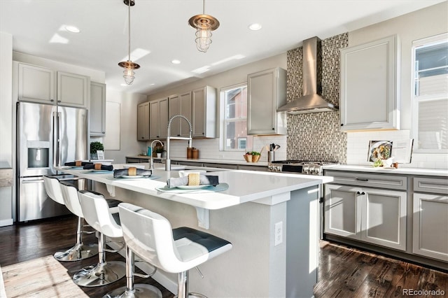 kitchen with pendant lighting, an island with sink, dark hardwood / wood-style flooring, stainless steel fridge with ice dispenser, and wall chimney exhaust hood