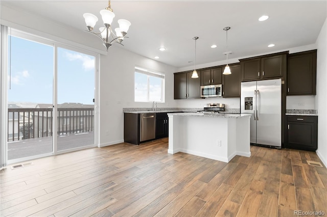 kitchen with hanging light fixtures, appliances with stainless steel finishes, light stone counters, and light wood-type flooring