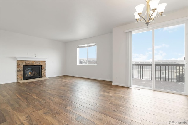 unfurnished living room with an inviting chandelier, a stone fireplace, and hardwood / wood-style floors